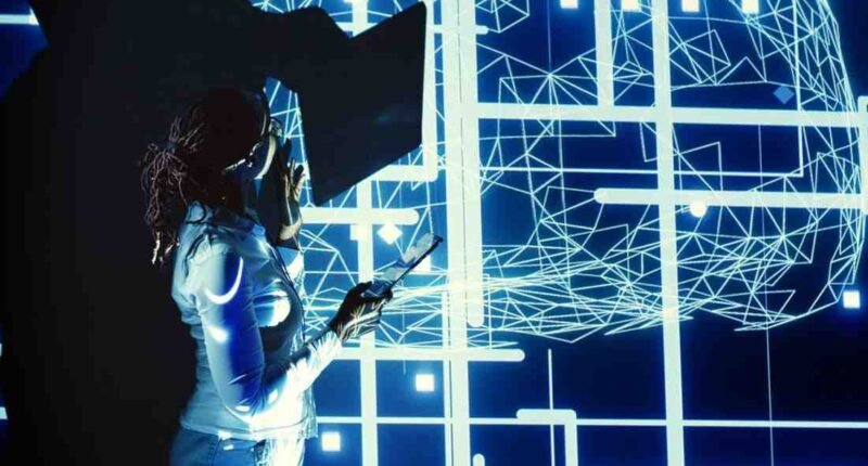 A person stands before a large screen displaying bright blue digital lines and grids, holding a tablet.